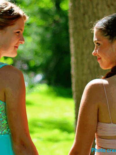 Two girls in prom dresses holding hands in the sunshine