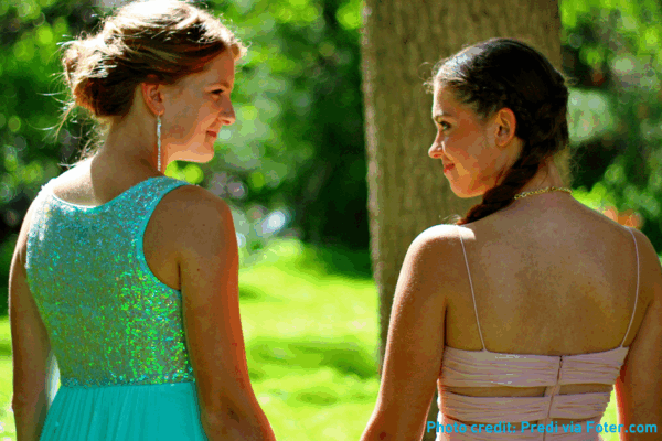 Two girls in prom dresses holding hands in the sunshine