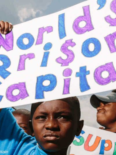 Photo of a young Black boy holding up a sign that reads "World's Prison Capital"