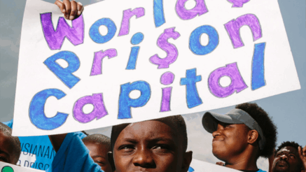 Photo of a young Black boy holding up a sign that reads "World's Prison Capital"