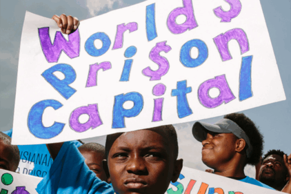 Photo of a young Black boy holding up a sign that reads "World's Prison Capital"