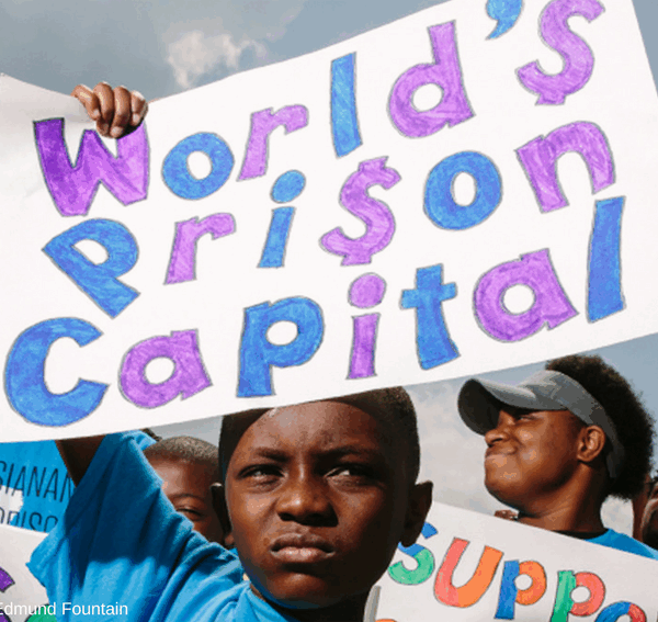 Photo of a young Black boy holding up a sign that reads "World's Prison Capital"