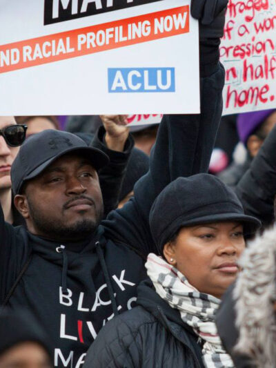 Black man holding a sign that reads "end racial profiling now"