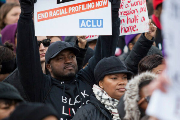 Black man holding a sign that reads "end racial profiling now"