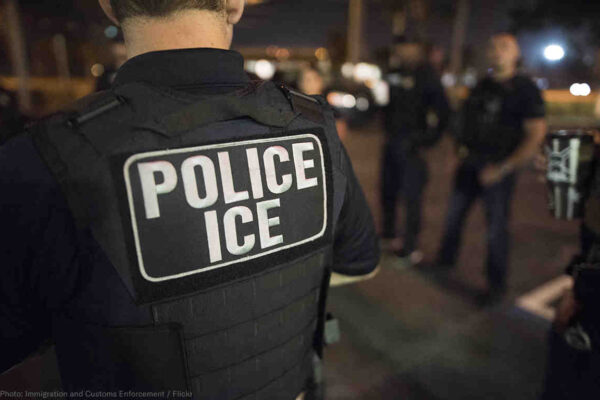 Officer wearing a flak jacket that reads "Police ICE"