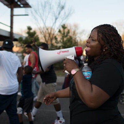 A Black woman speaking into a bullhorn at a protest