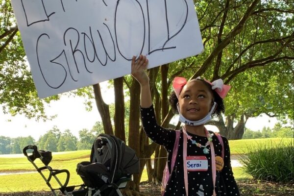 A young Black girl holding a sign reading "Let Me Grow Old"