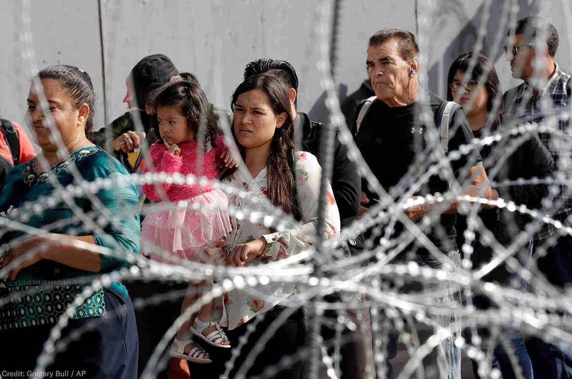 A line of immigrants behind a barbed wire fence 