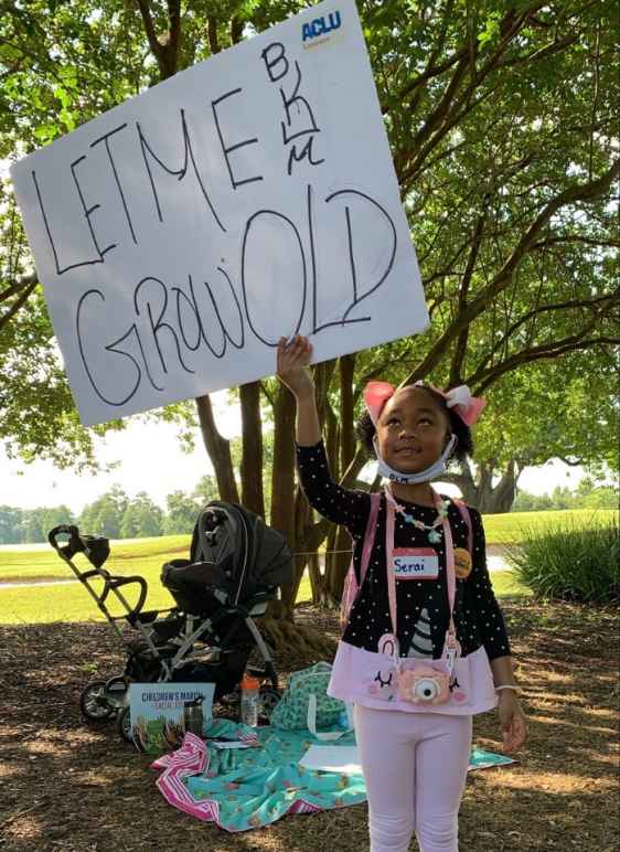 A young Black girl holding a sign reading "Let Me Grow Old"