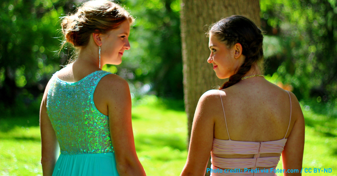 Two girls in prom dresses holding hands in the sunshine