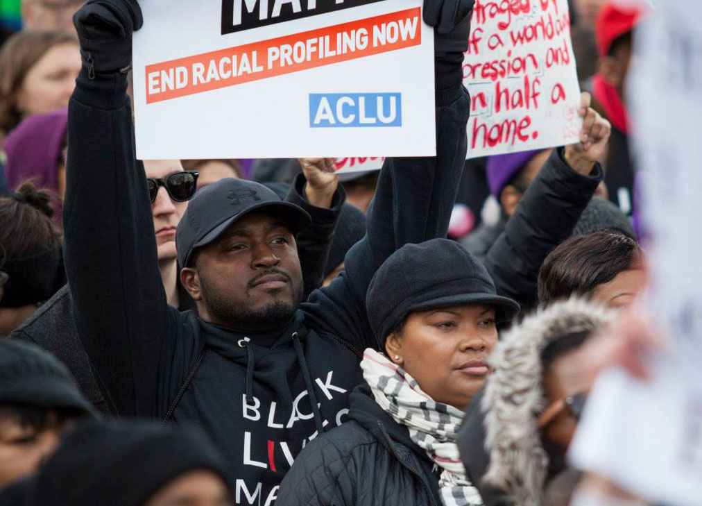 Black man holding a sign that reads "end racial profiling now"