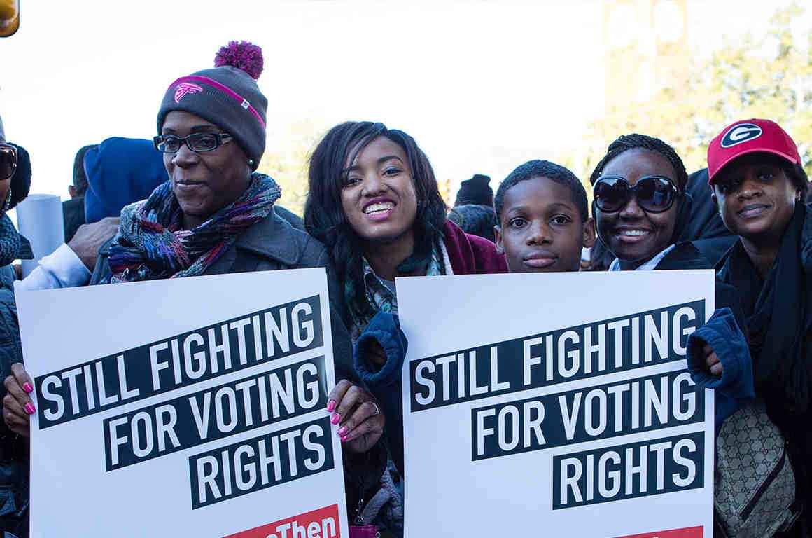 Group of Black young hold signs reading "Still fighting for voting rights"