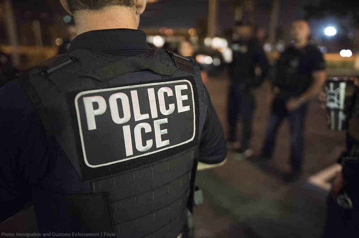 Officer wearing a flak jacket that reads "Police ICE"