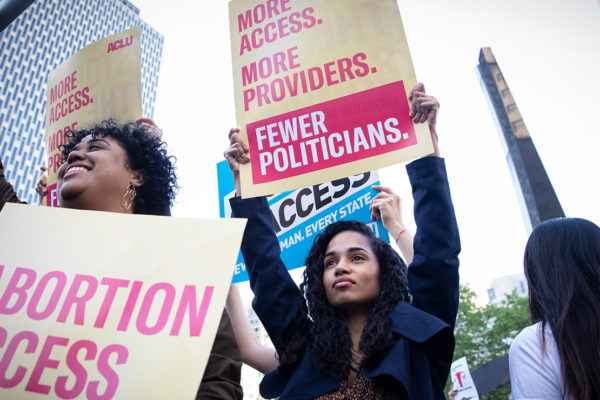 Woman holding a sign reading "More Access. More Providers. Fewer Politicians."