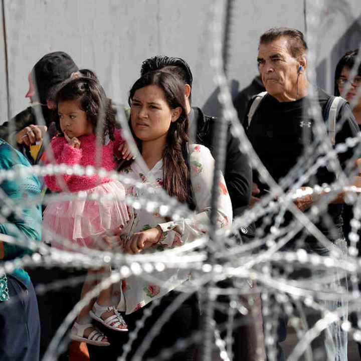 A line of immigrants behind a barbed wire fence 