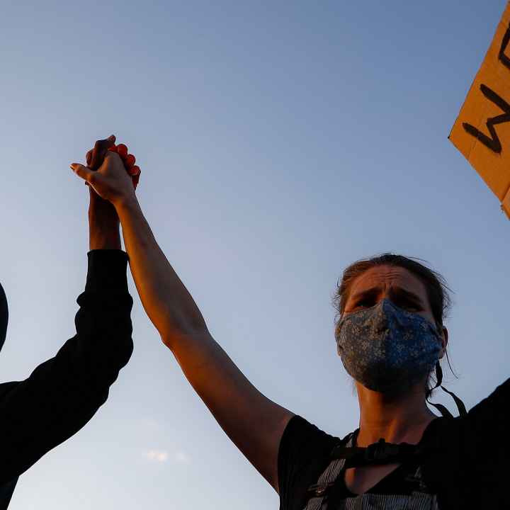 A black protester and a white protester hold hands while holding a sign that reads "We Can't Breathe"