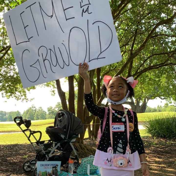 A young Black girl holding a sign reading "Let Me Grow Old"