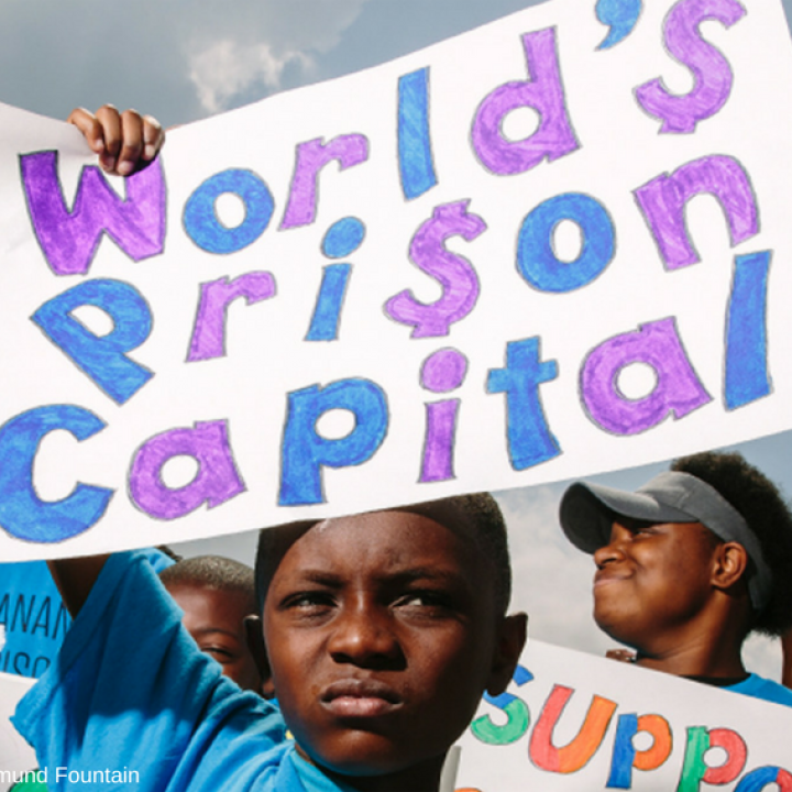 Photo of a young Black boy holding up a sign that reads "World's Prison Capital"