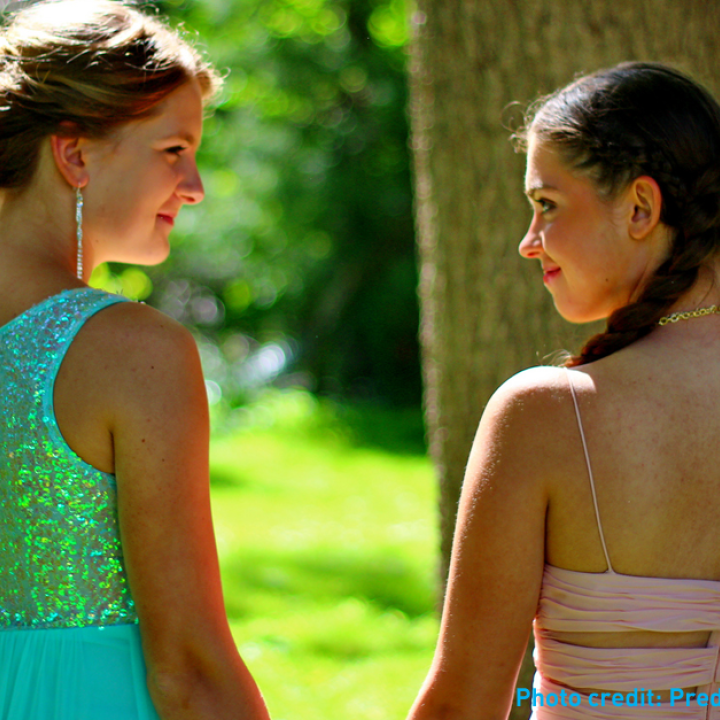 Two girls in prom dresses holding hands in the sunshine